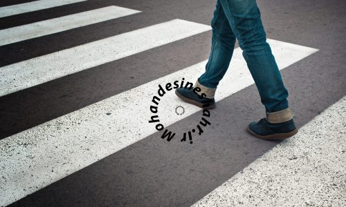Legs of young woman in jeans and leather boots crossing street on zebra marking